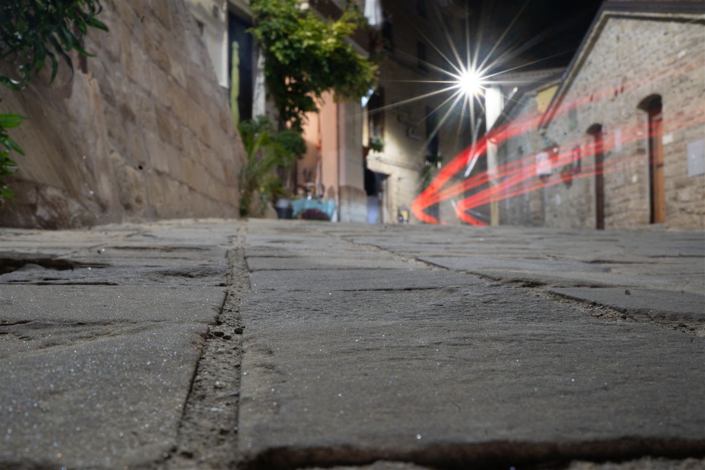 Basoli di pietra di una strada di Castelmezzano, di notte, con la scia luminosa di un'auto