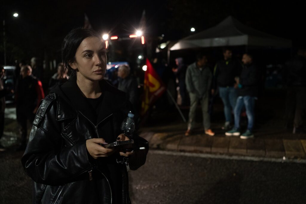Teresa Leone, giovane imprenditrice dei trasporti, in giacca di pelle nera al presidio di Rende di sera; alle sue spalle le luci di un camion, una bandiera rossa e gialla e altri manifestanti.